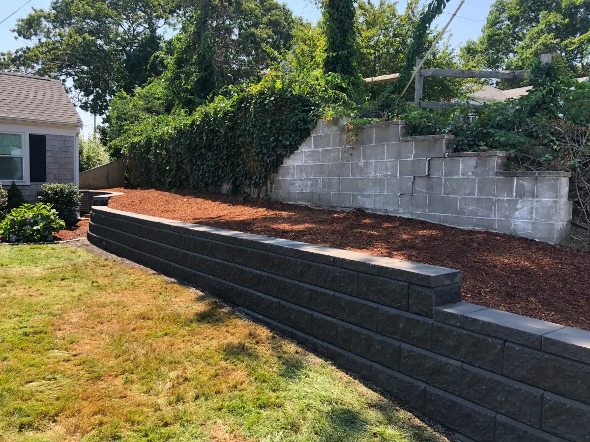 Charcoal segmental block retaining wall with capstones and a fresh mulch bed built by Braun Construction on Cape Cod