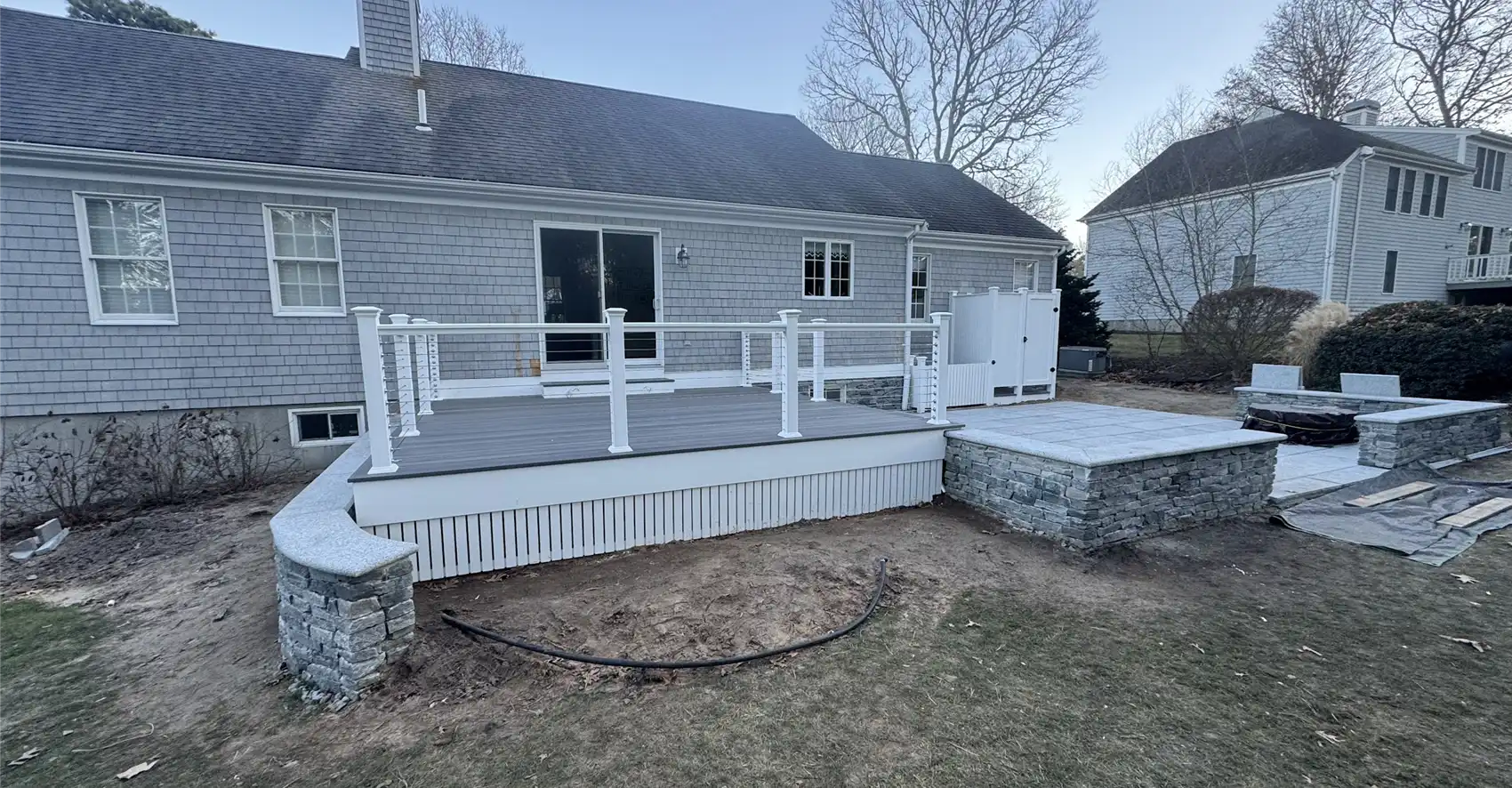 Raised composite deck with white cable railing and adjoining stone patio built by Braun Construction on Cape Cod