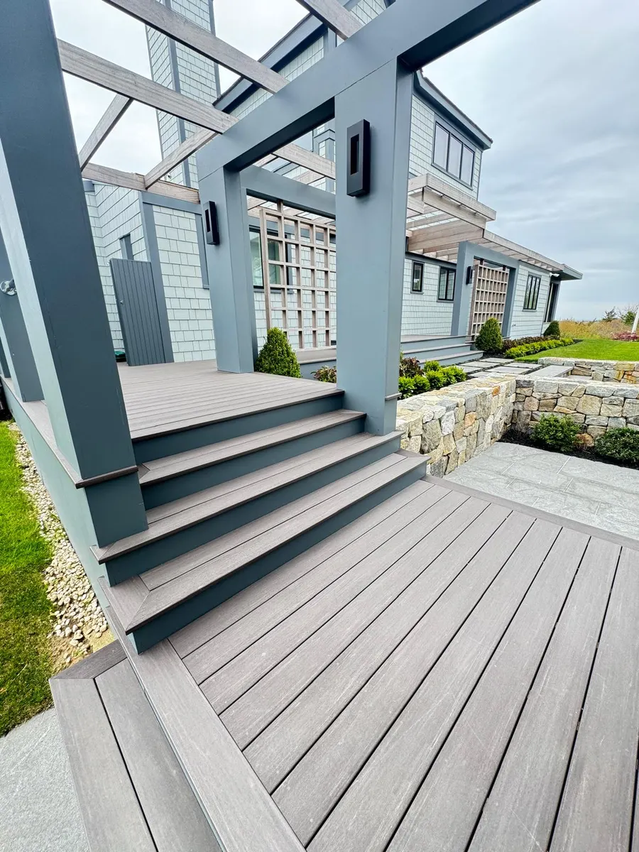 Composite deck with pergola, wide stairs and adjoining stone patio built by Braun Construction on Cape Cod