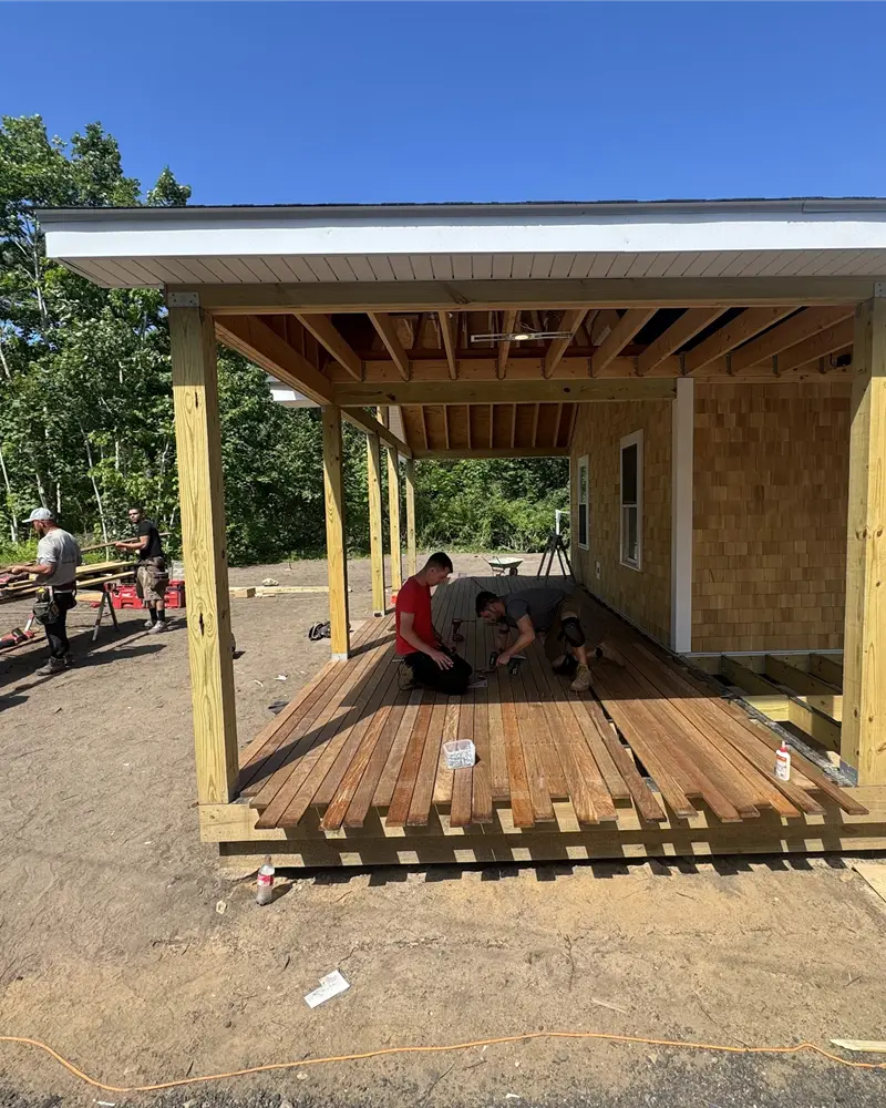 Braun Construction crew laying mahogany decking on a covered porch deck under a clear sky on Cape Cod