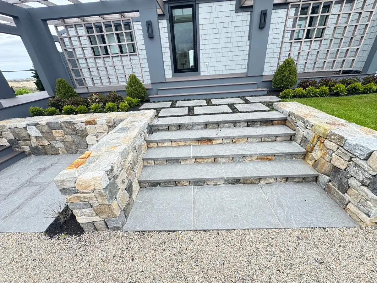 Granite steps between dry-laid fieldstone walls leading to a bluestone patio built by Braun Construction on Cape Cod