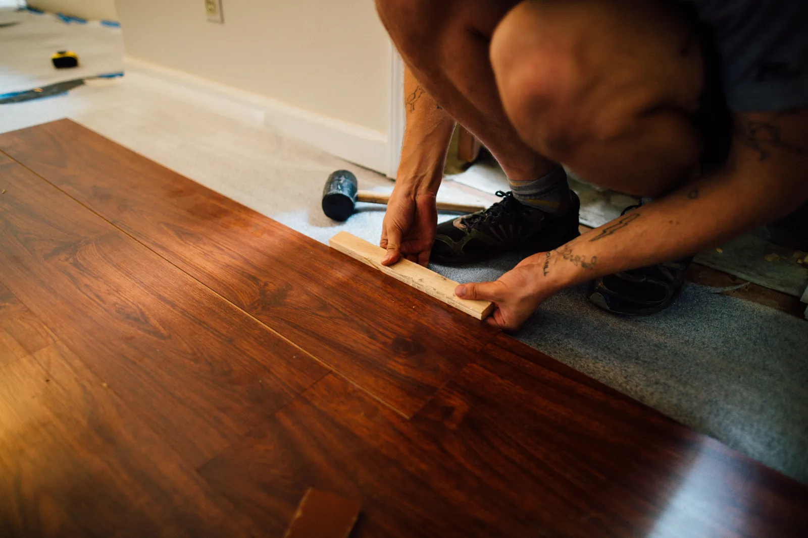 Installer tapping a laminate flooring plank into place with a tapping block during a floor installation