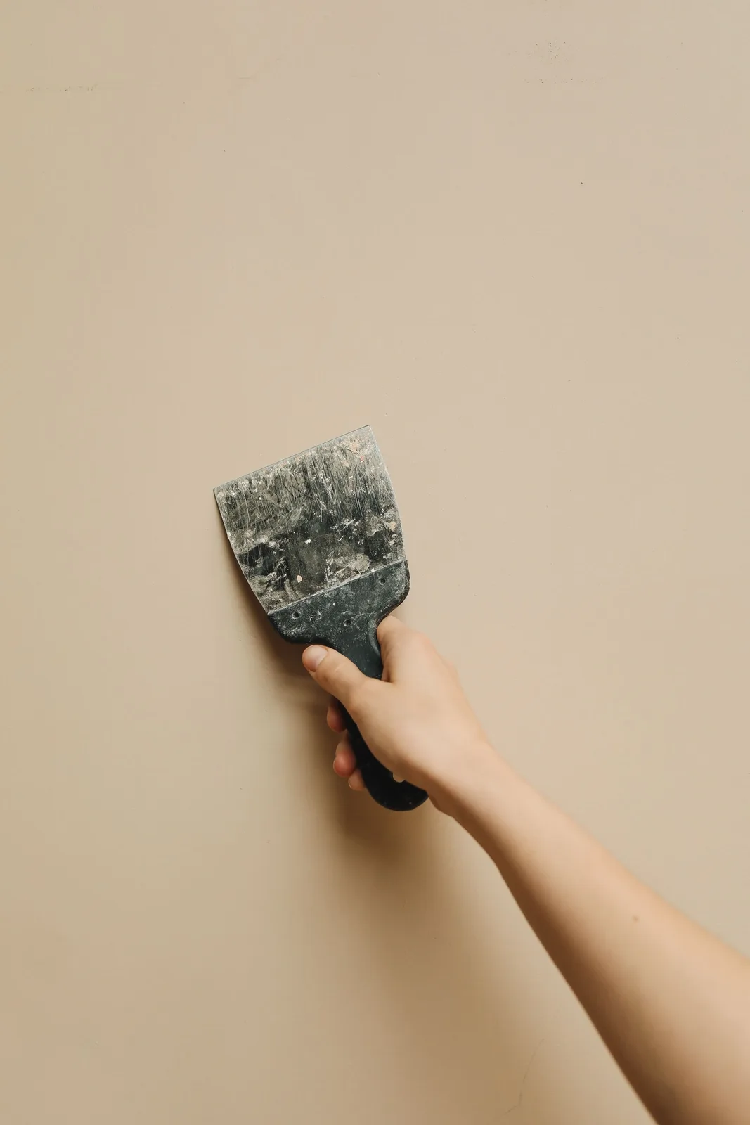 Putty knife held against a wall to scrape and strip old wall covering before drywall repair