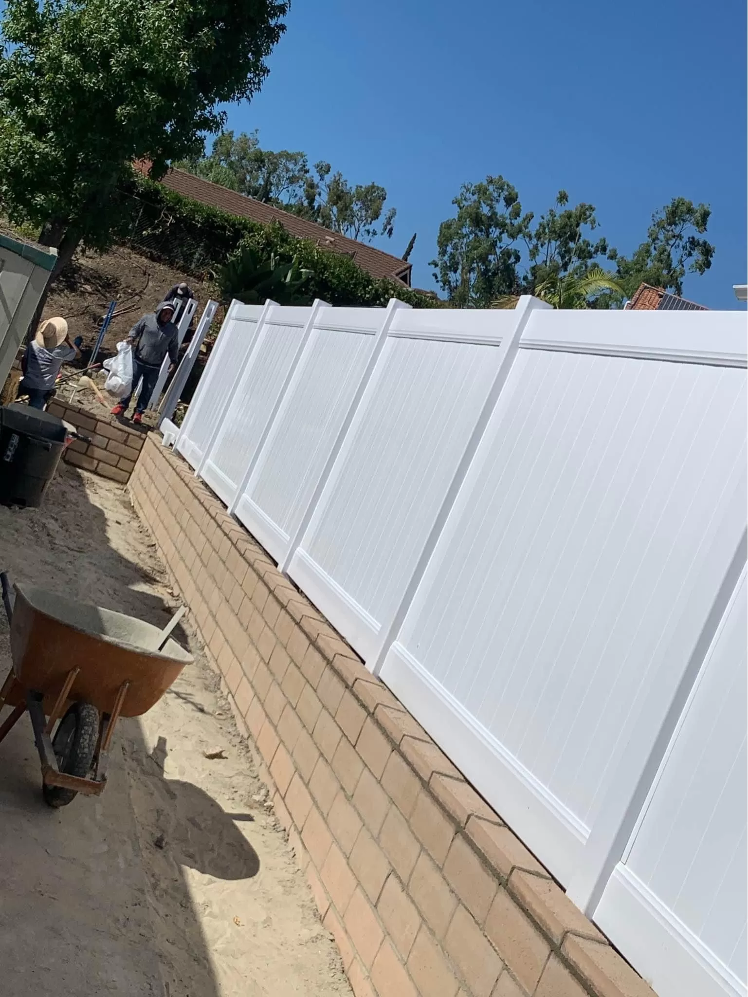White vinyl privacy fence installed on a brick retaining wall by Braun Construction in Centerville, MA